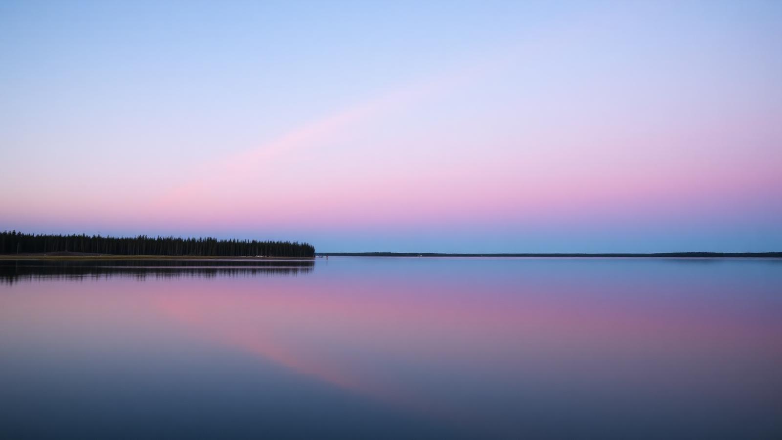 Calm Manitoba lake at dusk with a soft pastel sky reflected in still water and a low boreal forest in the distance.